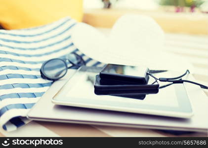 beach, summer vacation and technology concept - close up of tablet pc, notebook, smartphone and summer accessories on beach