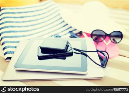 beach, summer vacation and technology concept - close up of tablet pc computer, smartphone, camera and summer accessories on beach