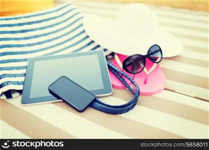 beach, summer vacation and technology concept - close up of tablet pc computer, smartphone and summer accessories on beach