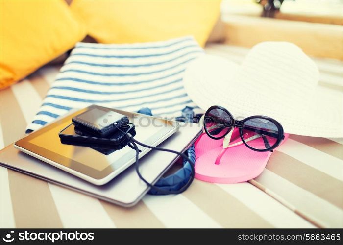 beach, summer vacation and technology concept - close up of tablet pc, notebook, smartphone and summer accessories on beach