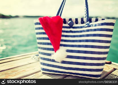 beach, summer, vacation, christmas and accessories concept - close up of beach bag and santa helper hat on wooden pier