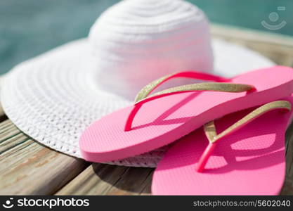 beach, summer, vacations and accessories concept - close up of hat and slippers at seaside