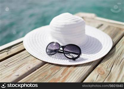 beach, summer, vacations and accessories concept - close up of hat and sunglasses at seaside