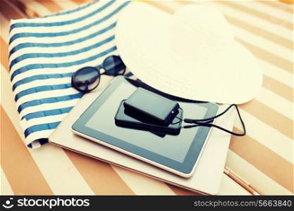 beach, summer vacations and technology concept - close up of tablet pc, notebook, smartphone and summer accessories on beach