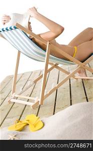 Beach - topless woman sitting on deckchair sunbathing with big white hat