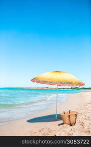 Beach umbrella with straw bag on the tropical beach. Beach umbrella on a sunny day with sea on background