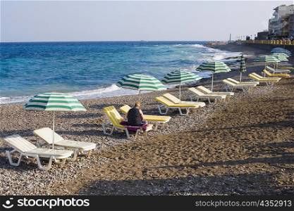Beach umbrellas and lounge chairs on the beach, Lindos, Rhodes, Dodecanese Islands, Greece