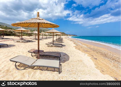 Beach umbrellas in rows for shade on sandy beach at coast with blue sea in Greece
