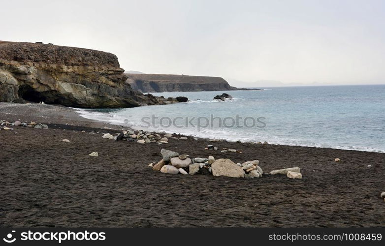 Beach with black sand near rocky coast in Ajuy village, Fuerteventura, Spain.