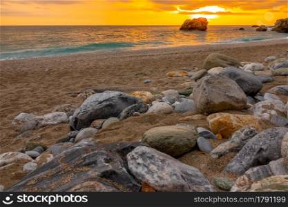 Beach with coarse sand and colorful stones. Golden sunset over the calm sea. Sunset Over the Calm Sea and Colorful Stones on the Sandy Beach