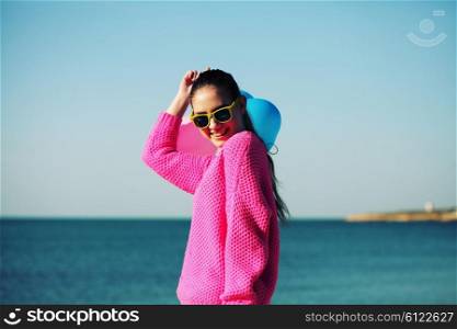 Beach woman laughing having fun in vacation holidays. Beautiful hipster girl dressed in bright youth clothes walking in the beach, holding colored balloons.