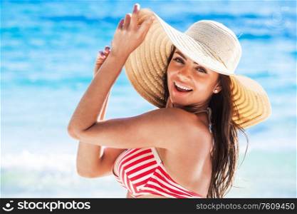 Beach woman relaxing on travel vacation smiling happy and cheerful in summer sun. Beautiful ?aucasian woman wearing white beach hat and bikini on tropical paradise beach.. Woman wearing beach hat