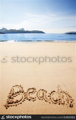 Beach written in the sand on the coast with mountains in the background