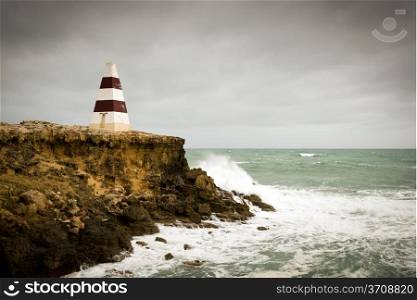 Beacon on a cliff top with waves crashing underneath a stormy sky