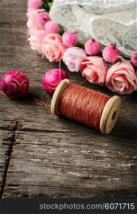Beads and spool of thread, piece of lace on textured wooden background