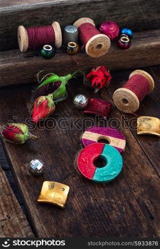 Beads,spools of thread on vintage wooden background decorated with rosebuds