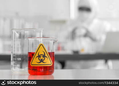 Beaker contains red liquid chemicals on a white laboratory table.