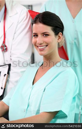 beaming brunette nurse sitting at desk with standing colleagues in background