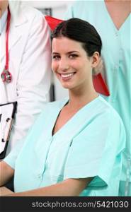 beaming brunette nurse sitting at desk with standing colleagues in background
