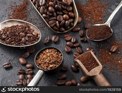 Bean and ground coffee and freeze dried instant coffee granules in various spoons and scoops on black background. Macro