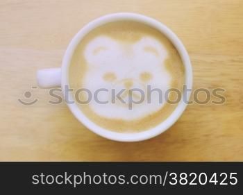 Bear latte art coffee cup on wooden table with retro filter effect