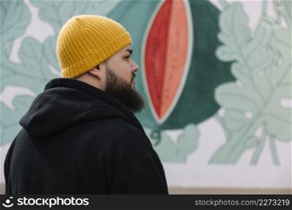 beard man wearing knit hat standing front graffiti wall