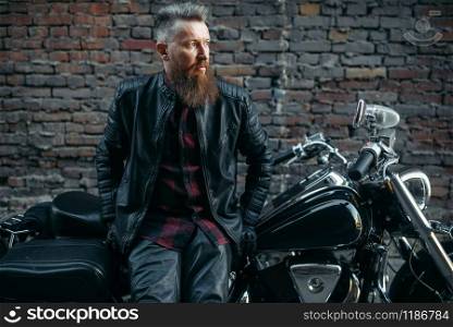 Bearded biker poses on classical chopper, two-wheeled transport. Vintage bike rider on motorcycle, freedom lifestyle