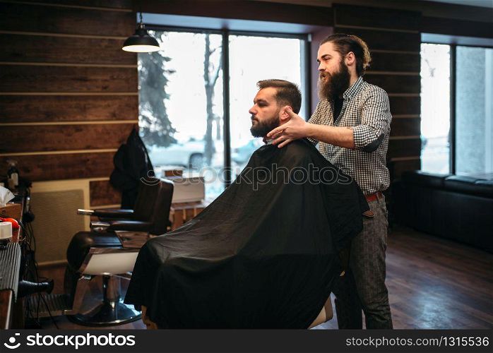 Bearded customer man in black salon cape visit barbershop. Coiffeur at work