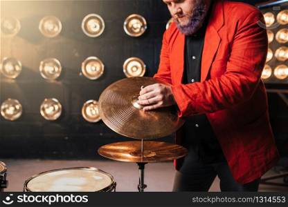 Bearded drummer in red suit on the stage with lights, retro style. Musical performer with colorful hair, drum instrument. Bearded drummer in red suit on the stage