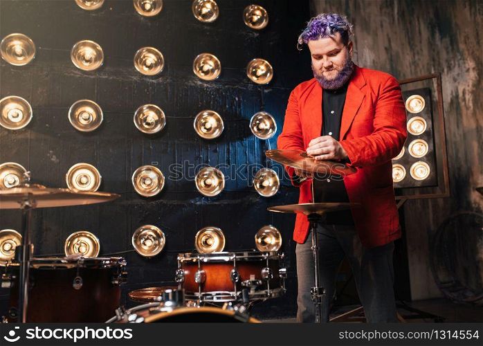 Bearded drummer in red suit on the stage with lights, retro style. Musical performer with colorful hair. Bearded drummer in red suit on the stage