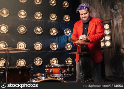Bearded drummer in red suit on the stage with lights, retro style. Musical performer with colorful hair. Bearded drummer in red suit on the stage