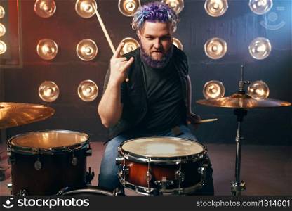 Bearded drummer with colorful hair, rock performer on the stage with lights, vintage style. Musical concert in night club. Bearded drummer with colorful hair, rock performer
