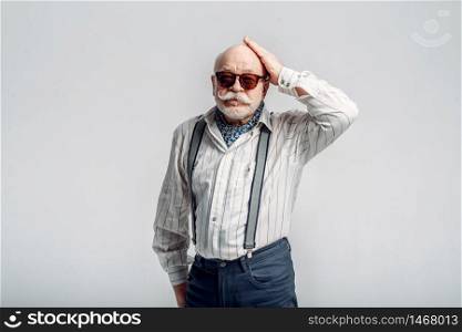 Bearded elderly man with mustache poses in sunglasses, grey background. Mature senior looking at camera. Elderly man with mustache poses in sunglasses