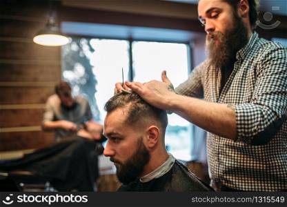 Bearded hairdresser making male hipster hairstyle. Client man in black salon cape visit barbershop. Bearded hairdresser making male hipster hairstyle