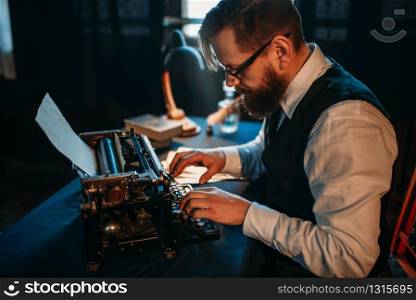 Bearded journalist in glasses typing on retro typewriter. Vintage lamp, feather, crystal decanter and books on background. Bearded journalist in glasses typing on typewriter