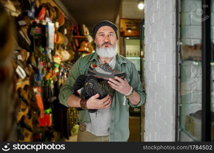 Bearded male hunter choosing boots in gun store. Weapon shop interior, rifles and ammunition assortment, firearms choice, shooting hobby and lifestyle. Bearded male hunter choosing boots in gun store