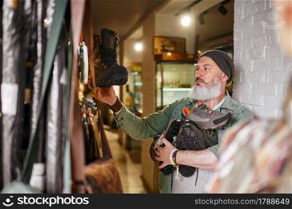 Bearded male hunter choosing boots in gun store. Weapon shop interior, rifles and ammunition assortment, firearms choice, shooting hobby and lifestyle. Bearded male hunter choosing boots in gun store