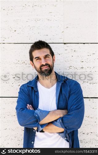 Bearded male leaning on wall with crossed arms while looking camera with a smile