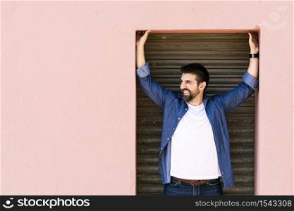 Bearded male standing against pink wall with arms raised while looking away