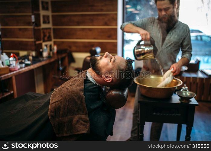 Bearded man at the barbershop, barber pours water into a copper bowl on background