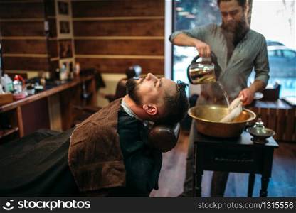 Bearded man at the barbershop, barber pours water into a copper bowl on background