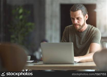 Bearded man Designer using laptop for making online reservation in the cafe. Hipster freelancer working a job at restaurant