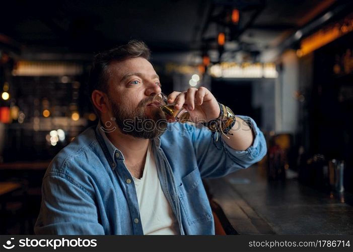 Bearded man drinks alcohol beverage at the counter in bar. One male person resting in pub, human emotions, leisure activities, nightlife. Bearded man drinks alcohol beverage in bar