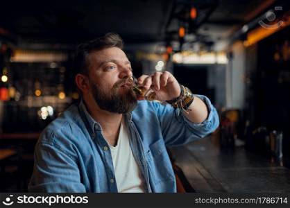 Bearded man drinks alcohol beverage at the counter in bar. One male person resting in pub, human emotions, leisure activities, nightlife. Bearded man drinks alcohol beverage in bar