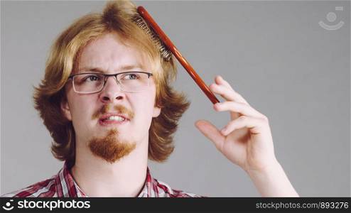 Bearded man having trouble with combing his hair using brush. Male haircare problems concept.. Man having problem with brushing hair