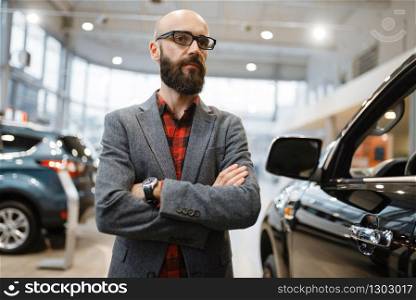 Bearded man in glasses poses at the pickup truck in car dealership. Customer in vehicle showroom, male person buying transport, auto dealer business. Bearded man poses at pickup truck, car dealership