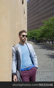 Bearded man, model of fashion, in urban background wearing casual clothes while leaning on a office building wall