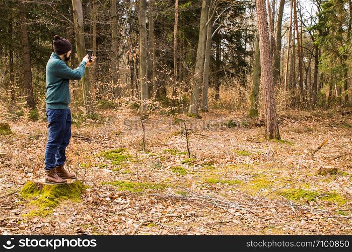 bearded man taking photo with smartphone in the forest