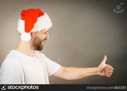 Bearded man wearing santa claus hat giving thumb up ok sign, on grey with copy space. Christmes time.. Man in santa claus hat giving thumb up