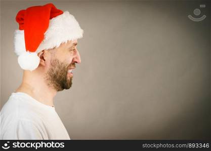 Bearded man wearing santa claus hat, side view on grey with copy space. Christmes time.. Bearded man in santa claus hat